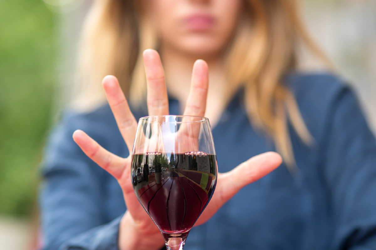 Une personne qui exprime un refus de consommer de l'alcool en brandissant sa main devant un verre de vin